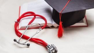 A graduation cap, a medical book and a stethoscope are placed on top of a table