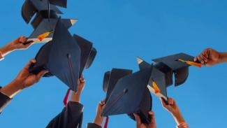Bursary funded students celebrating their graduation by throwing their graduation caps in the air