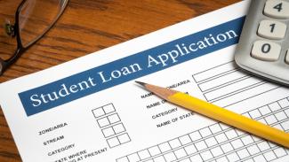 A fill-in student loan application form on top of a table with a pencil and calculator